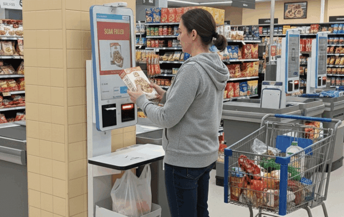 A woman scans groceries at a self-checkout kiosk in a supermarket, highlighting the risk of barcode switching fraud during automated checkout processes.
