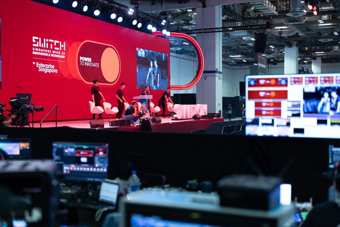 Behind-the-scenes view of the singapore switch stage, showcasing the "power to innovate" theme at the singapore week of innovation & technology. Event staff prepare for a presentation as technical equipment and monitors are set up in the foreground.