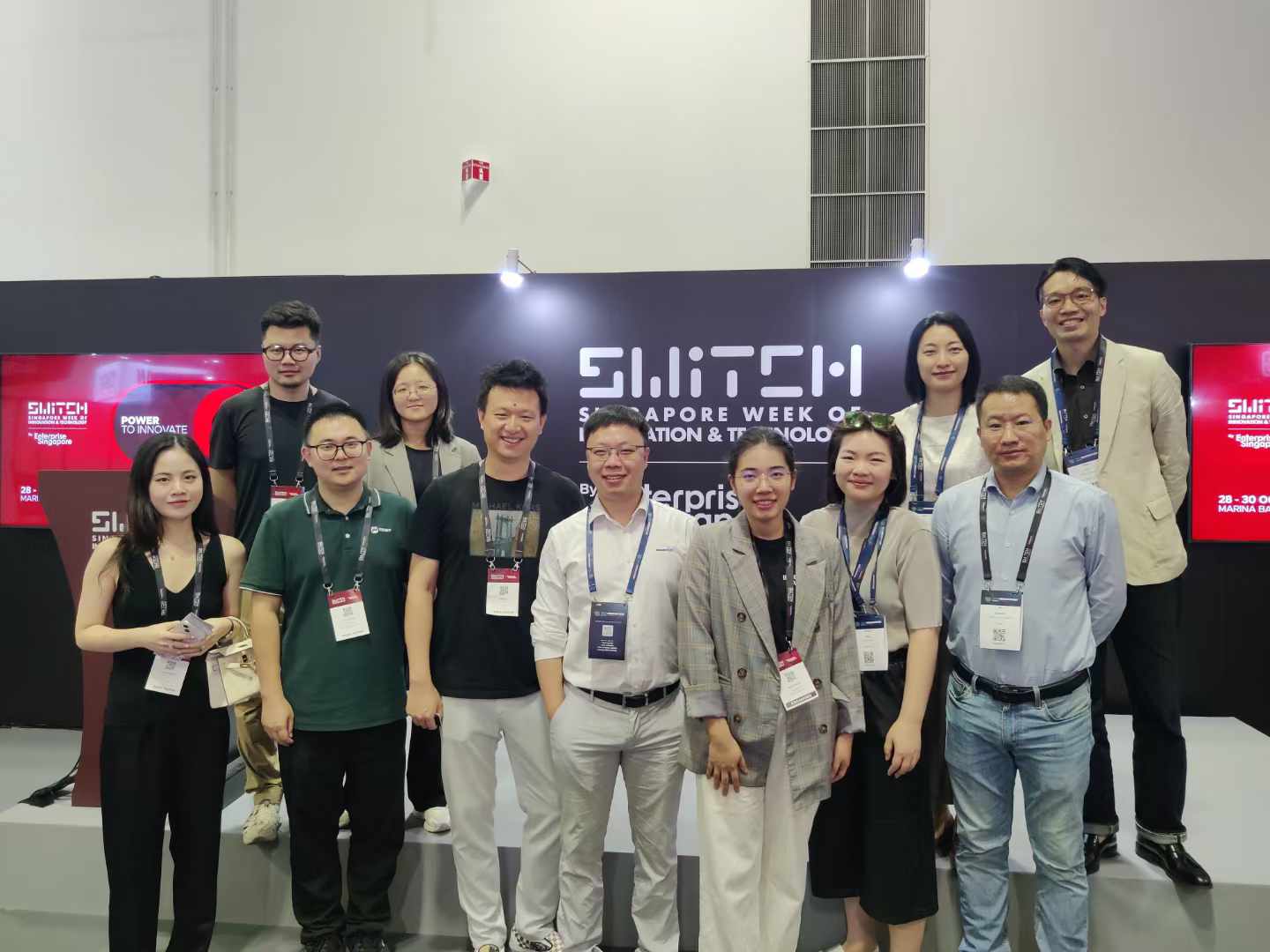 A group of professionals poses for a photo at the singapore switch event, part of the singapore week of innovation and technology. Attendees are wearing lanyards and badges, standing in front of the official switch backdrop with the theme "power to innovate. " the event showcases innovation and technology advancements in singapore.