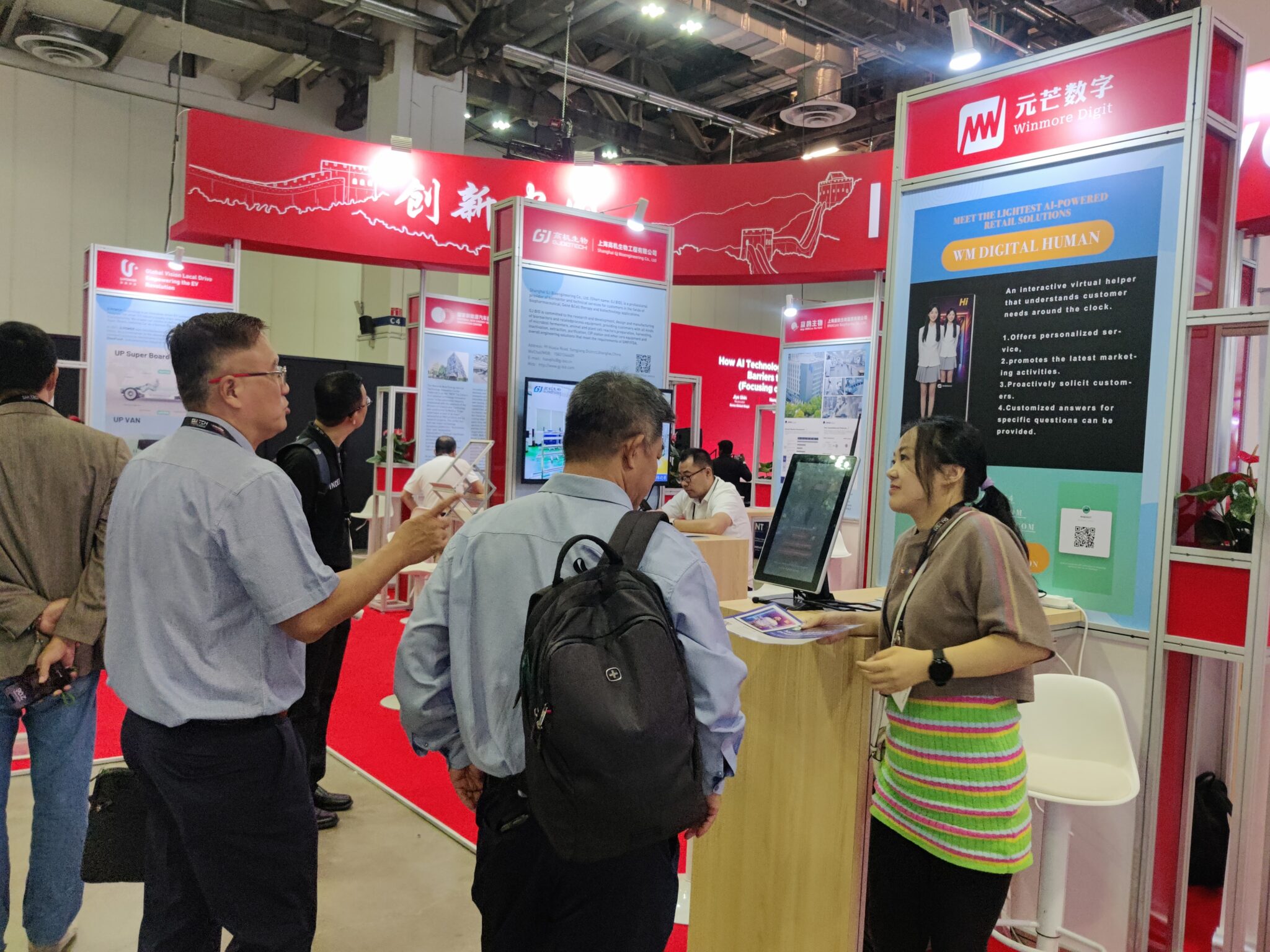 Winmore digital booth at a technology exhibition, showcasing ihuman — an ai-powered virtual assistant for retail innovation. Visitors engage with staff to learn about intelligent customer service solutions.