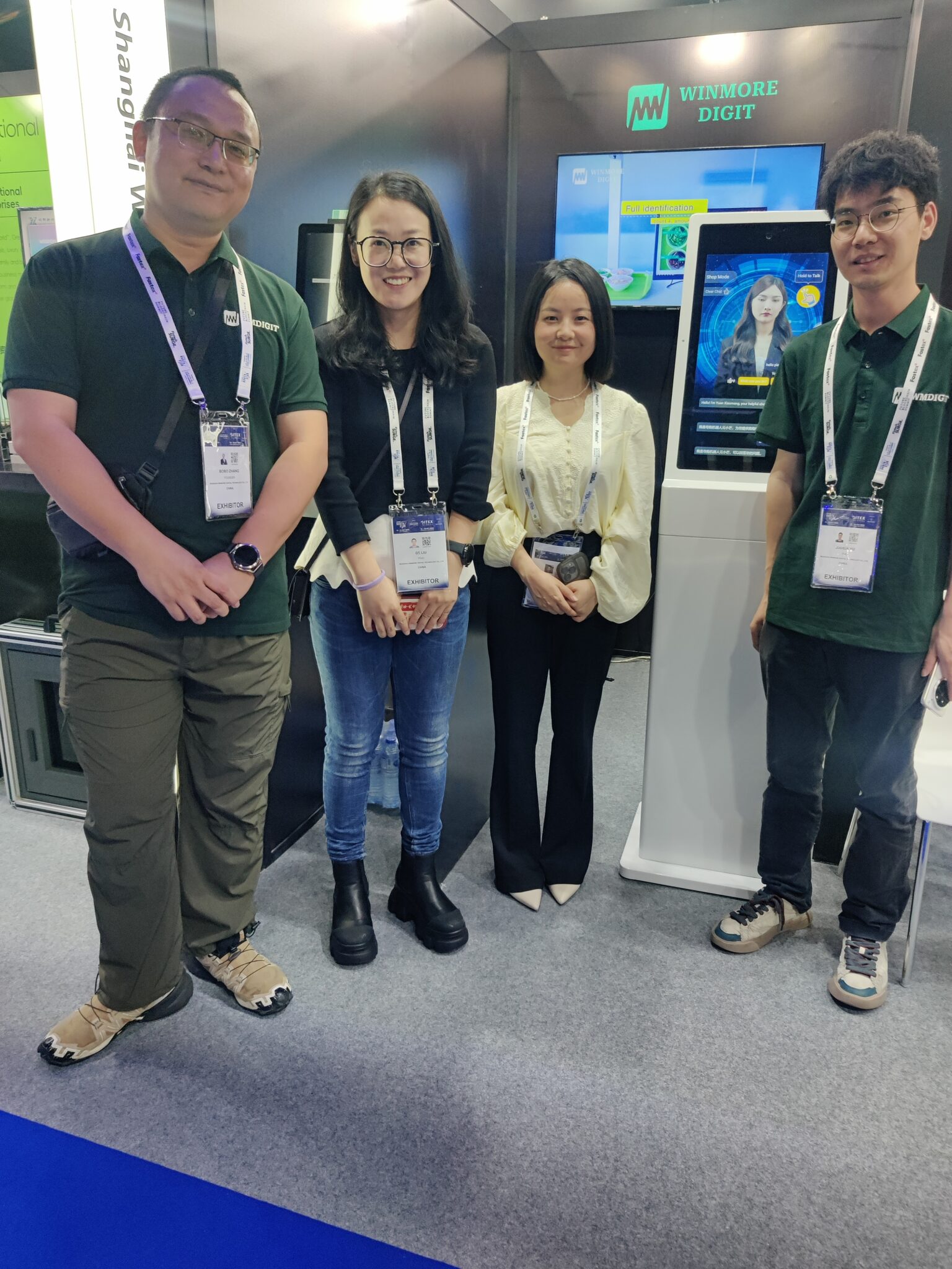 Team members from winmore digit smile confidently at their booth during gitex, standing beside an ai-powered kiosk that highlights their innovative digital solutions.