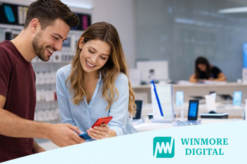 A smiling sales associate and customer interact at a retail counter, using smartphones to explore personalized shopping experiences powered by a retail ai solution.